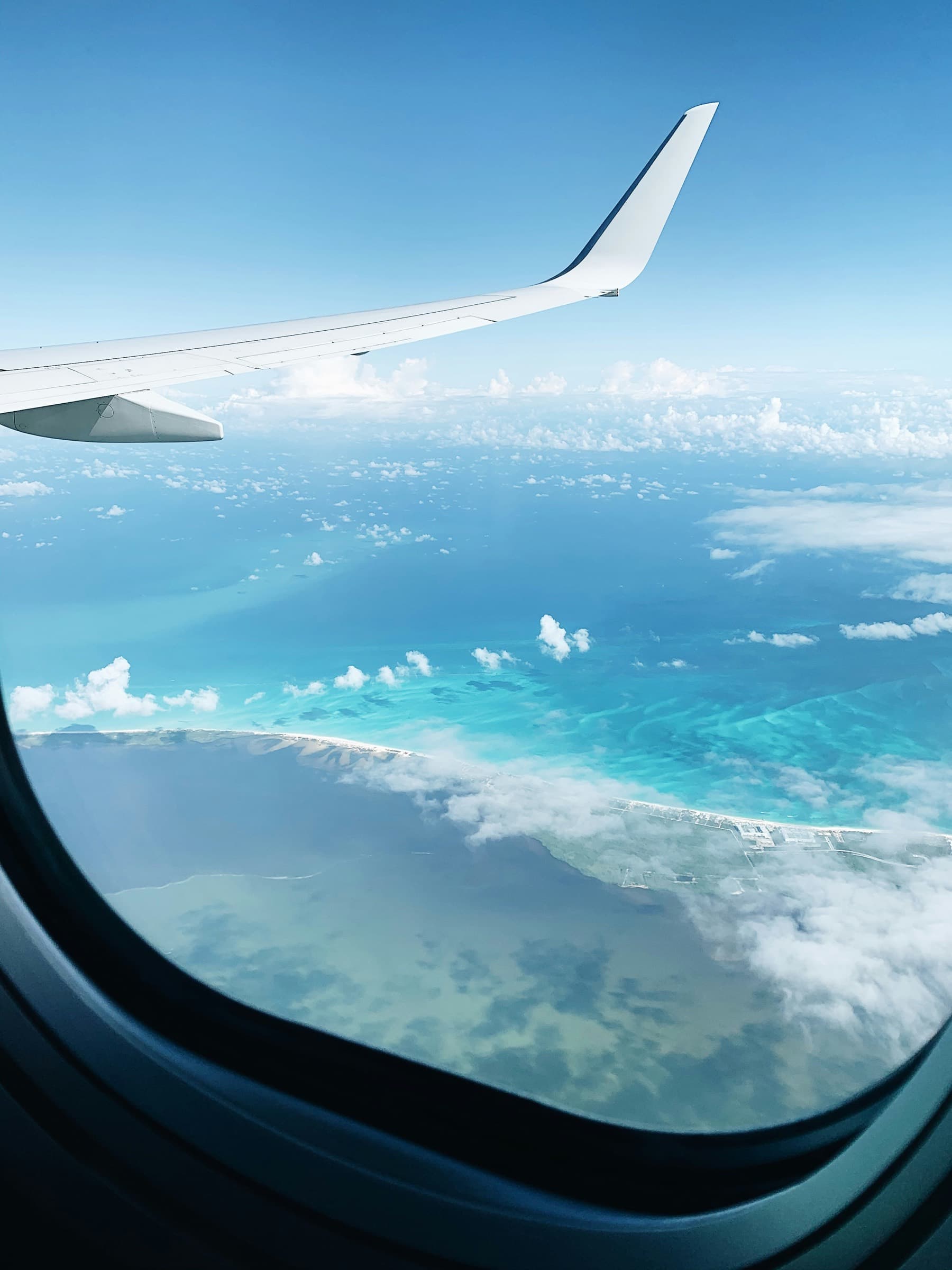 La vista desde la ventanilla de un avión: un ala sobre aguas turquesa y una costa blanca y delgada.